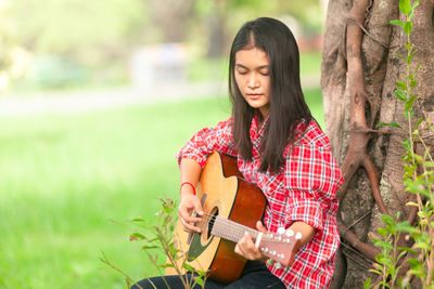 Woman playing guitar against tree