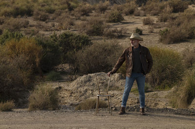 Adult man in cowboy hat with abandoned chair in desert, almeria, spain