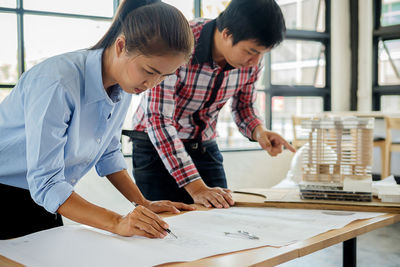 Colleagues analyzing blueprint on table in office