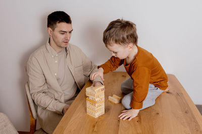 Father and son sitting together at home and playing with wooden blocks. jenga game.