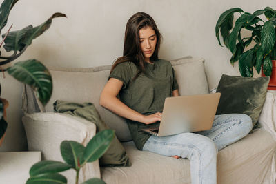 Young woman using laptop while sitting on sofa at home