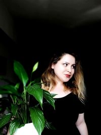 Smiling woman looking away by plant in darkroom