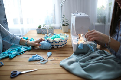 Beautiful woman with long dark hair sews blue cloth on sewing machine.