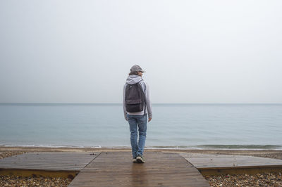 Rear view of man standing at beach against clear sky