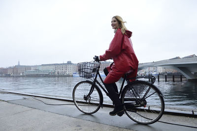 Denmark, copenhagen, happy woman riding bicycle at the waterfront in rainy weather