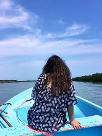 Rear view of woman siting on boat in sea against blue sky