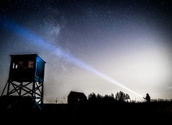 Silhouette woman holding flashlight by tower against star field on land