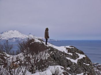 Person standing on snow covered rock formation against sky