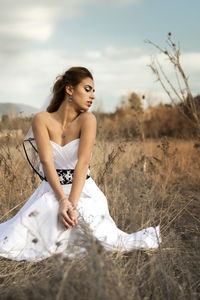 Young woman looking away while sitting on land