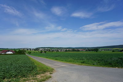 Road by agricultural field against sky