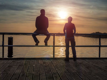 Couple of tourists. a woman leans over the railing and looks at the sunset over the sea. sea bridge