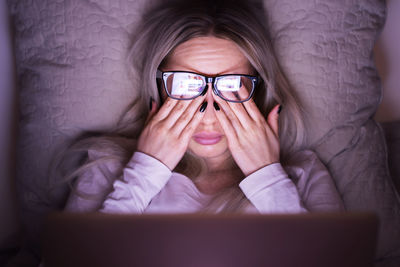 Sleepy woman in glasses rubbing eyes, feels tired after working on laptop, lying on pillow. overwork