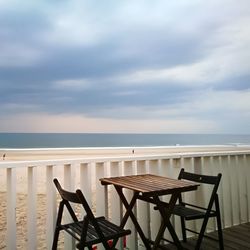 Chairs and table by sea against sky