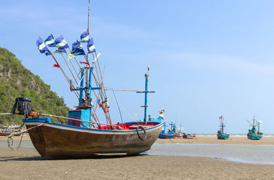 Sailboats moored on beach against blue sky