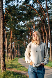 Portrait of a young blond woman walking in a pine forest at dawn.