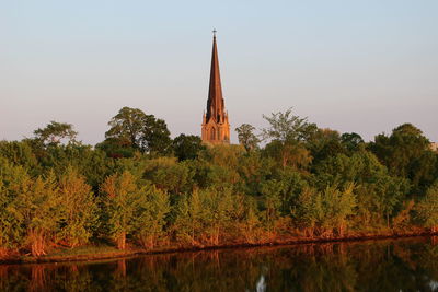 River by trees and cathedral against clear sky