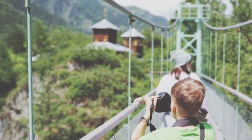 Rear view of boy photographing while standing on footbridge