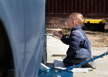 A little boy fixes a car, changes a wheel, helps his dad.