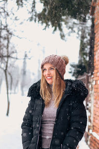 Smiling young woman standing in snow during winter