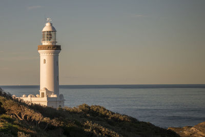 Lighthouse by sea against sky during sunset