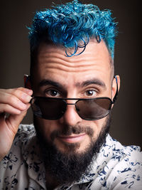Close-up portrait of man with dyed hair wearing sunglasses against black background
