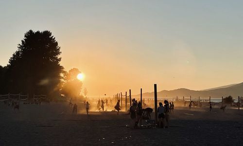 People at beach against sky during sunset