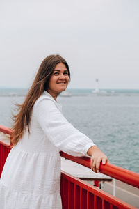 Portrait of smiling woman standing by railing against sea