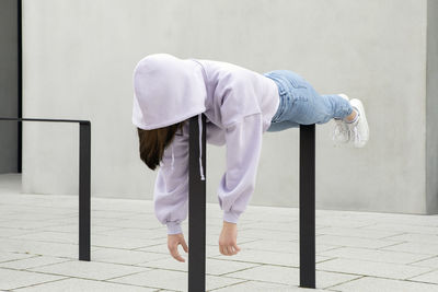 Girl in hooded shirt lying on metal by wall