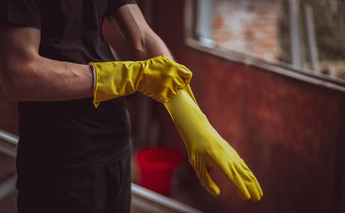 Young caucasian man puts yellow rubber gloves on his hands getting ready to wash window frames