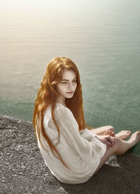 Beautiful young woman sitting by lake