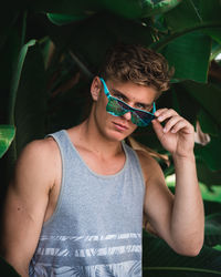 Portrait of young man wearing sunglasses standing against plants