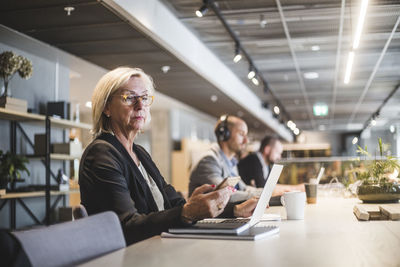 Senior businesswoman using mobile phone while working at table with colleagues in office