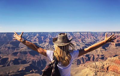 Rear view of teenage girl with arms outstretched standing on mountain against clear blue sky