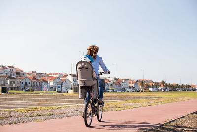 Rear view of woman riding bicycle while carrying son on road against sky