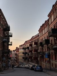 Cars on road by buildings against sky during sunset