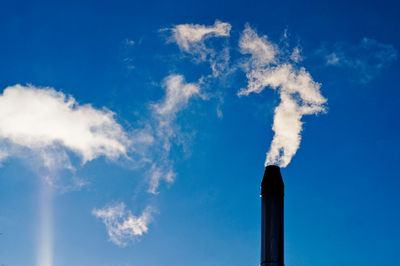 Low angle view of smoke emitting from chimney against blue sky