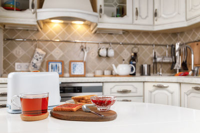 White toaster, cup of black tea, stack of toasted bread, crispy toast with raspberry jam