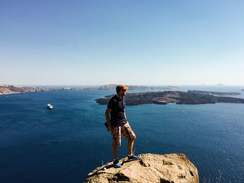 Man standing on rock by sea against clear sky