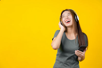 Smiling young woman using mobile phone against yellow background