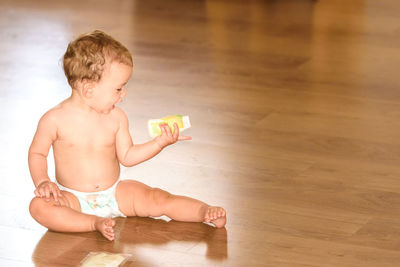 Shirtless baby girl sitting on hardwood floor