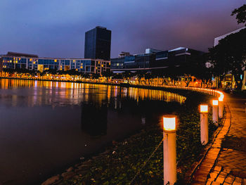 Illuminated buildings by river against sky at night