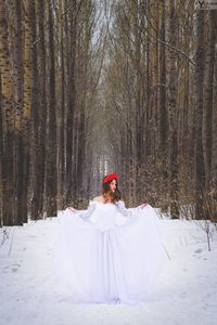 Female model posing in white dress amidst bare trees during winter