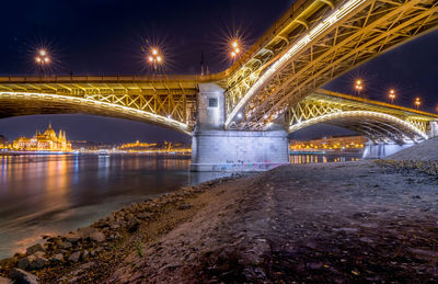 Illuminated bridge over river in city at night