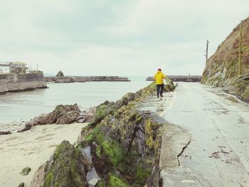 Rear view of man walking on road by sea against sky