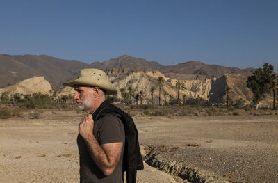 Adult man in cowboy hat on tabernas desert with palm trees against blue sky. almeria, spain