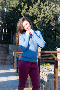 Full length of a smiling young woman standing against trees