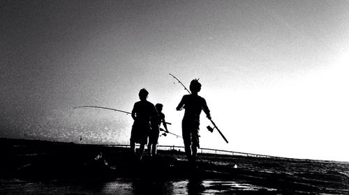 Silhouette men fishing on beach against clear sky