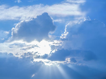 Low angle view of sunlight streaming through clouds