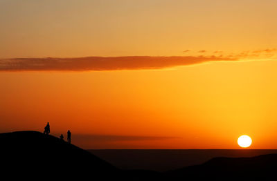 Silhouette people standing on sand dune at erg chebbi desert against sky during sunset