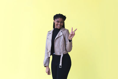 Portrait of young woman standing against yellow background